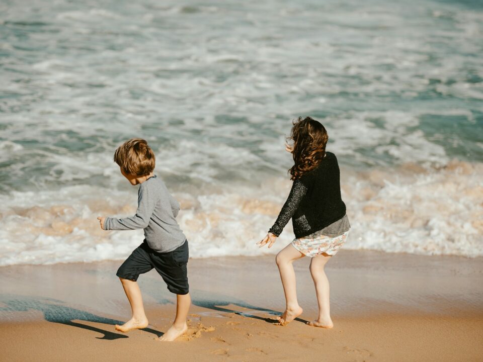 two young children playing on the beach near the ocean